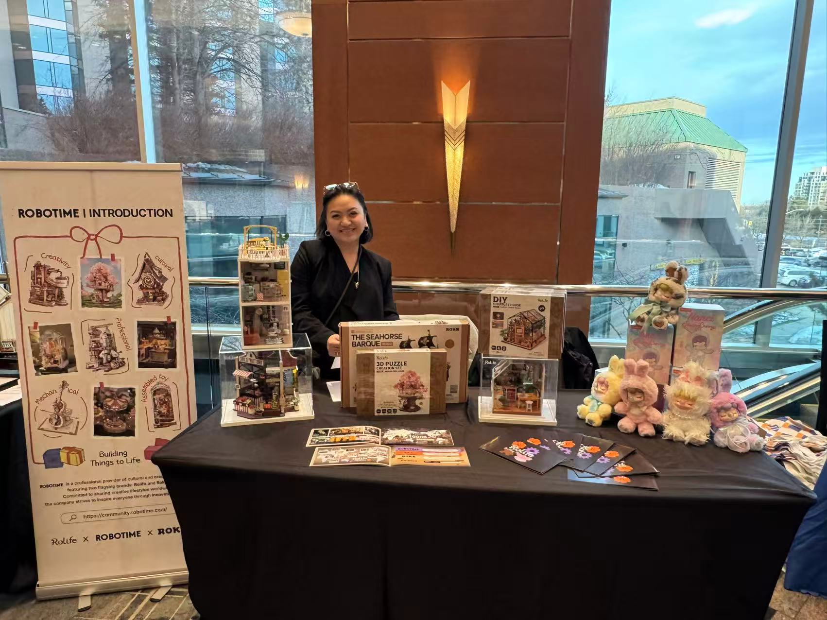 Miriam Reina behind a table with promotional materials and products in an indoor setting.