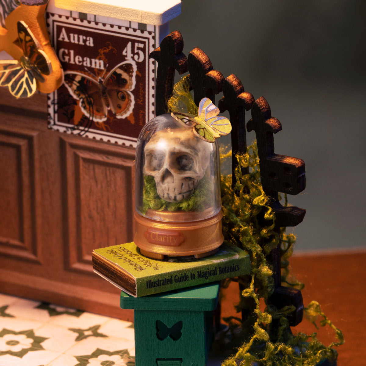 Rolife Potions Workshop DS057 close-up of skull under a glass dome on botanical books with butterfly detail and moss-covered gate