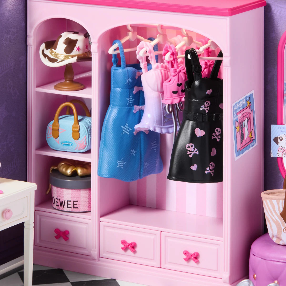 Pink miniature wardrobe with hanging blue, pink and black dresses, shelves holding a cow-print hat, blue handbag and round box, plus drawers with pink bow handles.