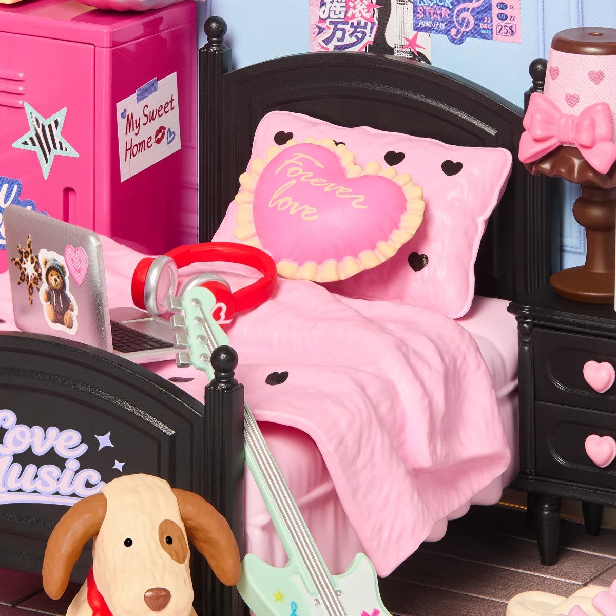 Close-up of a Rolife miniature bedroom showing a black bed with pink bedding, heart-shaped Forever Love pillow, red headphones, laptop, guitar and dog figure.