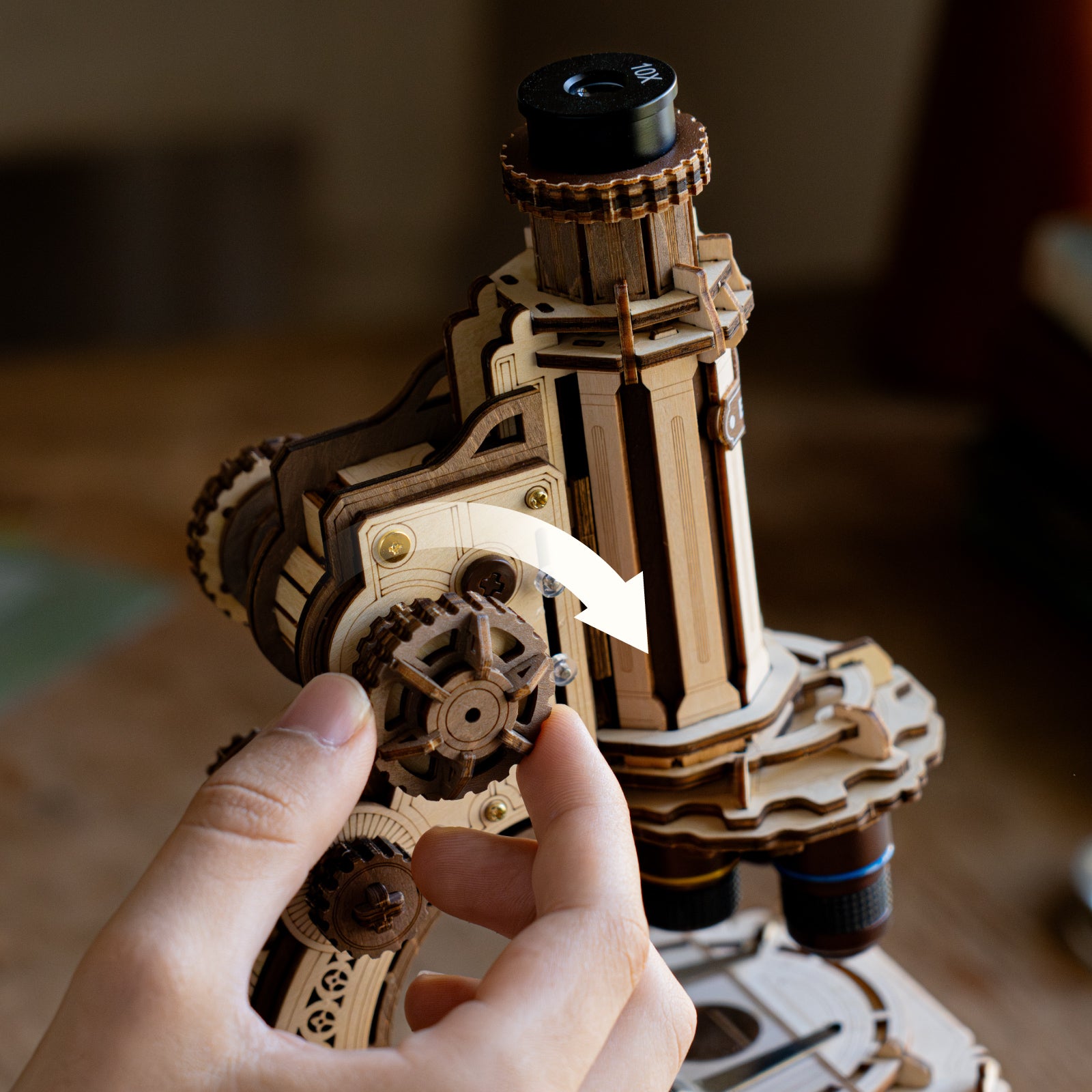 Hand holding the cylindrical barrel of the ROKR wooden microscope showing fine gear and lathe-turned wooden detail