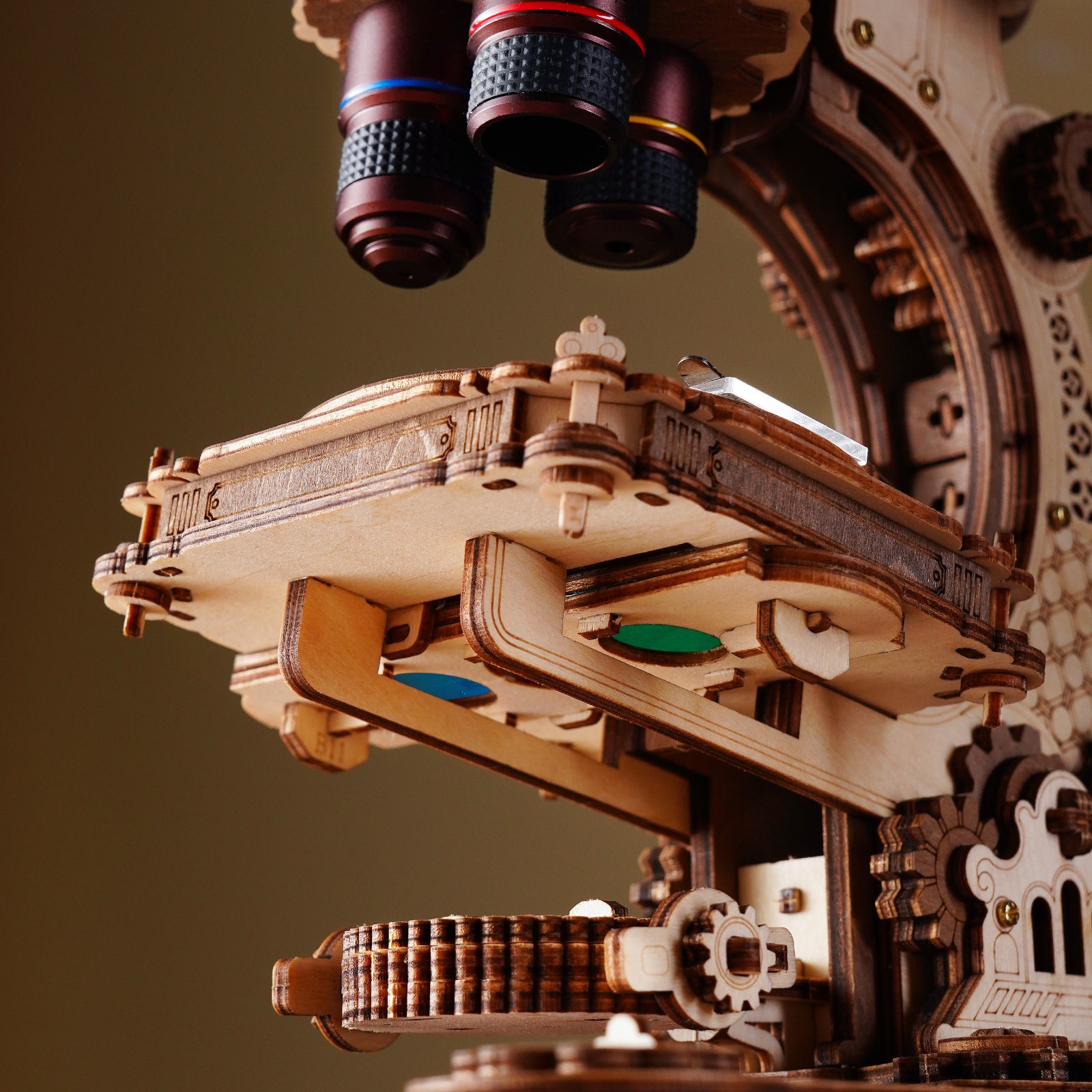 Close-up macro view of the ROKR wooden microscope revolving nosepiece showing blue and red objective lens rings and gear teeth