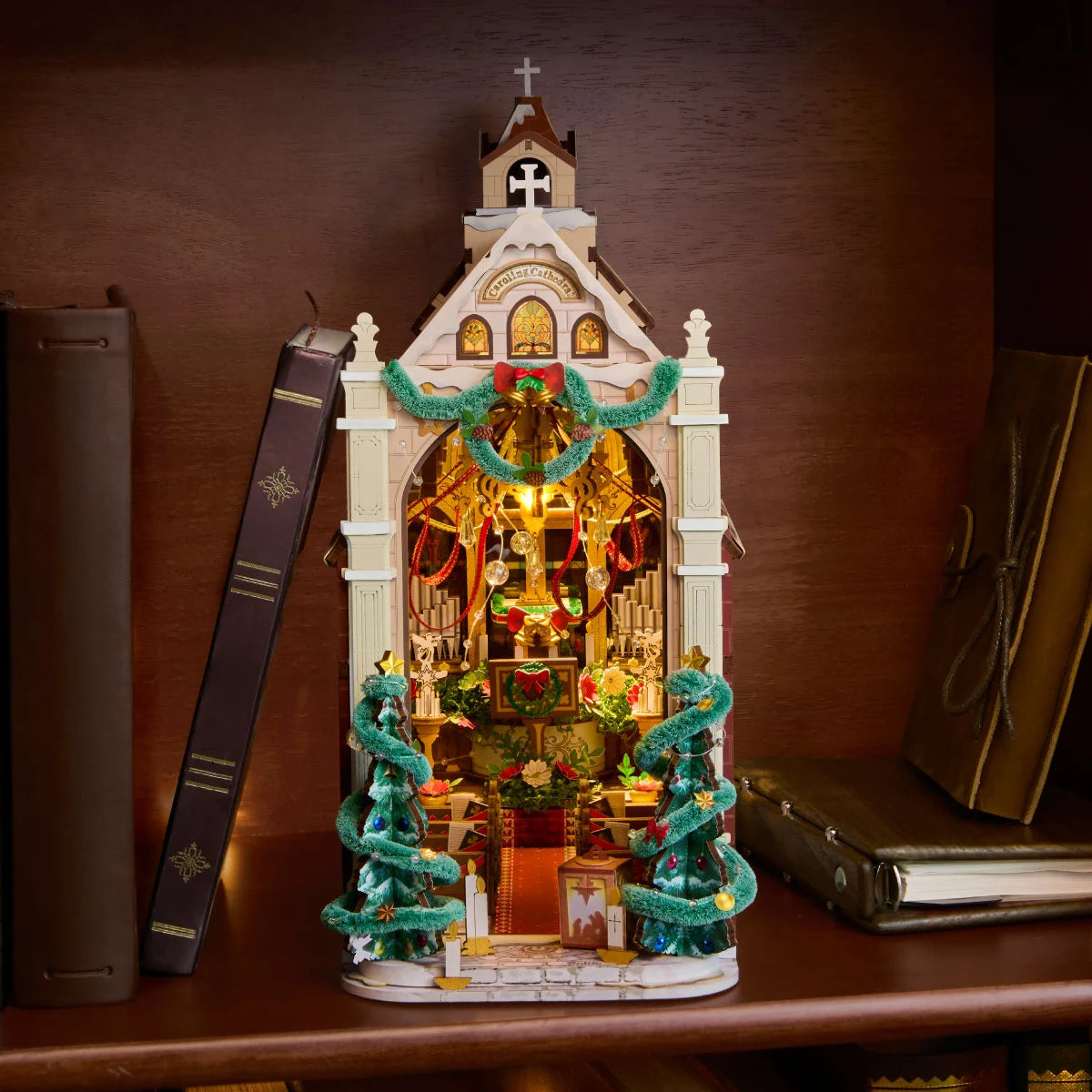Rolife miniature Christmas cathedral displayed on a wooden shelf between upright books, its arched interior illuminated with warm light.