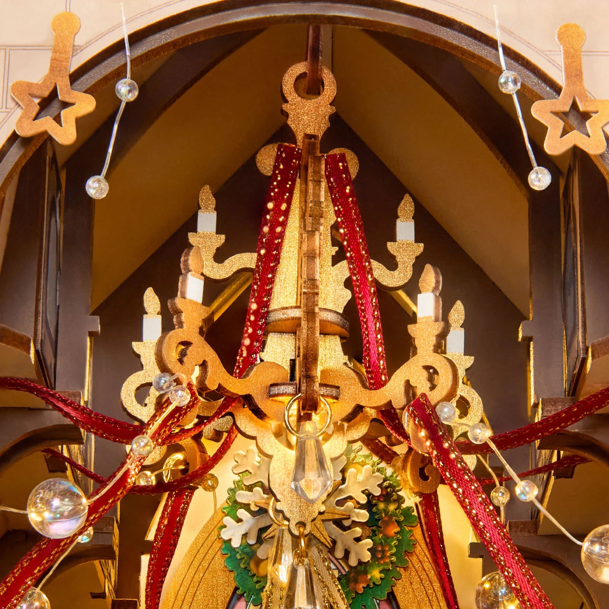 Close-up of a miniature cathedral interior showing a gold chandelier with candle shapes, red ribbons, clear beads and a green wreath.