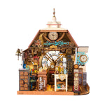 Rolife miniature clock shop diorama with red roof, large Roman numeral clock face, ornate blue scrollwork, wooden cabinets, workbench and tiny clocks on a wooden base.