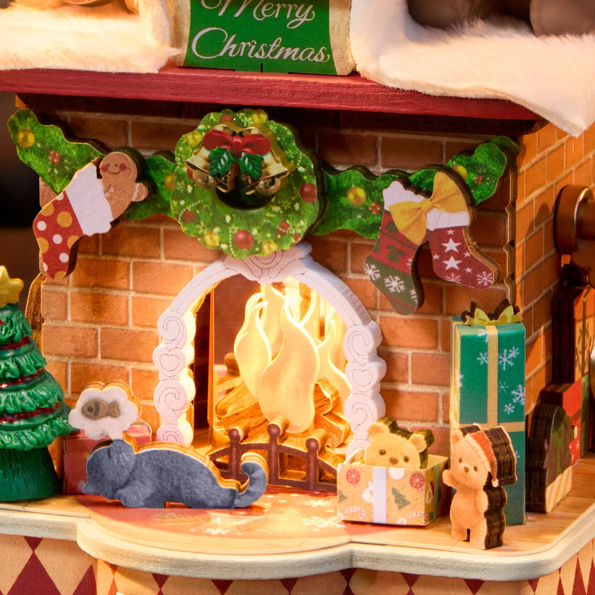 Close-up of the Rolife fireplace front showing a glowing arched fire, brick texture, wreath with bells, stockings, miniature tree, grey cat and teddy bear figures.