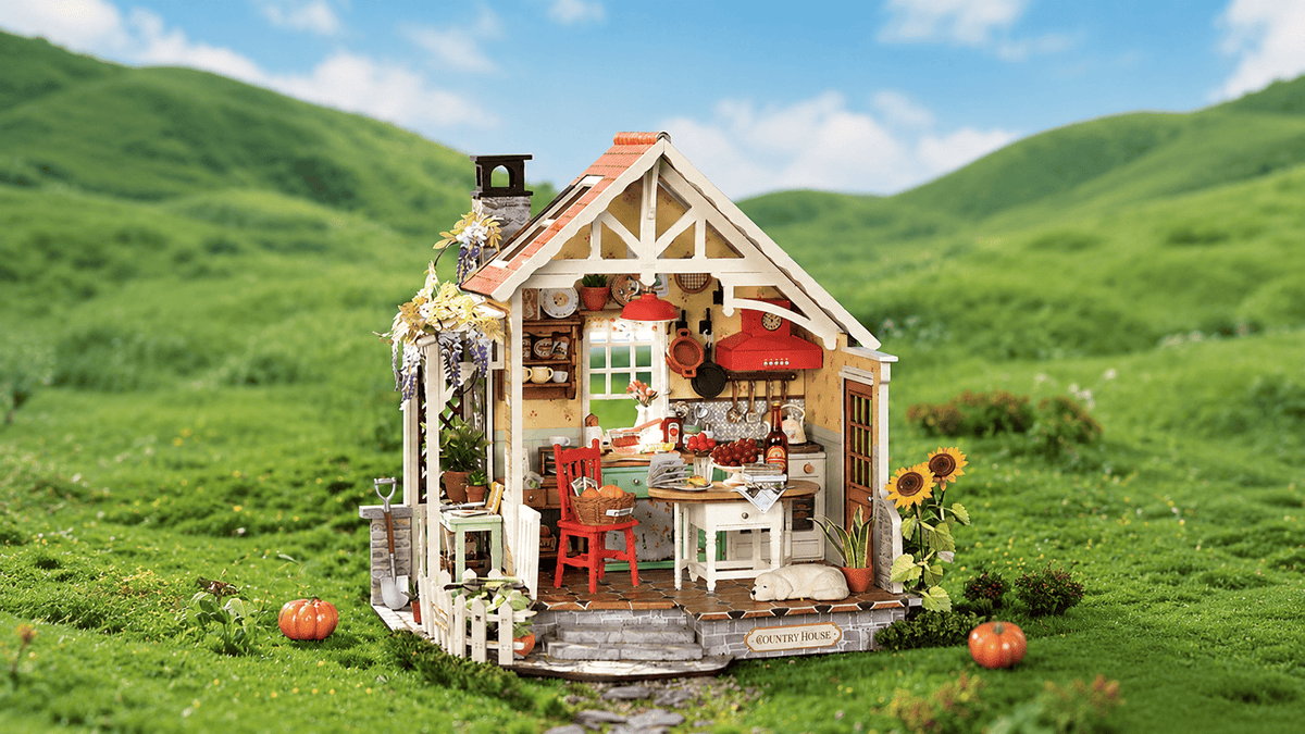 Rolife miniature house with open glass walls showing the kitchen interior on a green hillside with pumpkins.