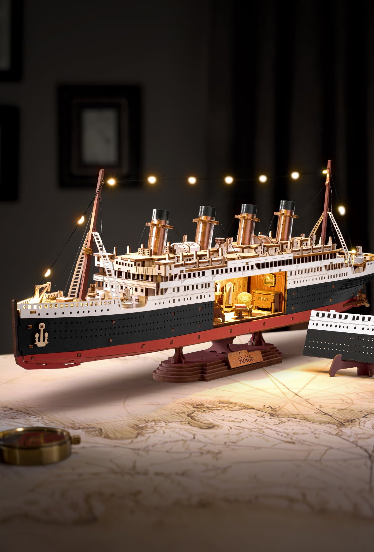 Illuminated wooden ocean liner model displayed above maps in a dark room