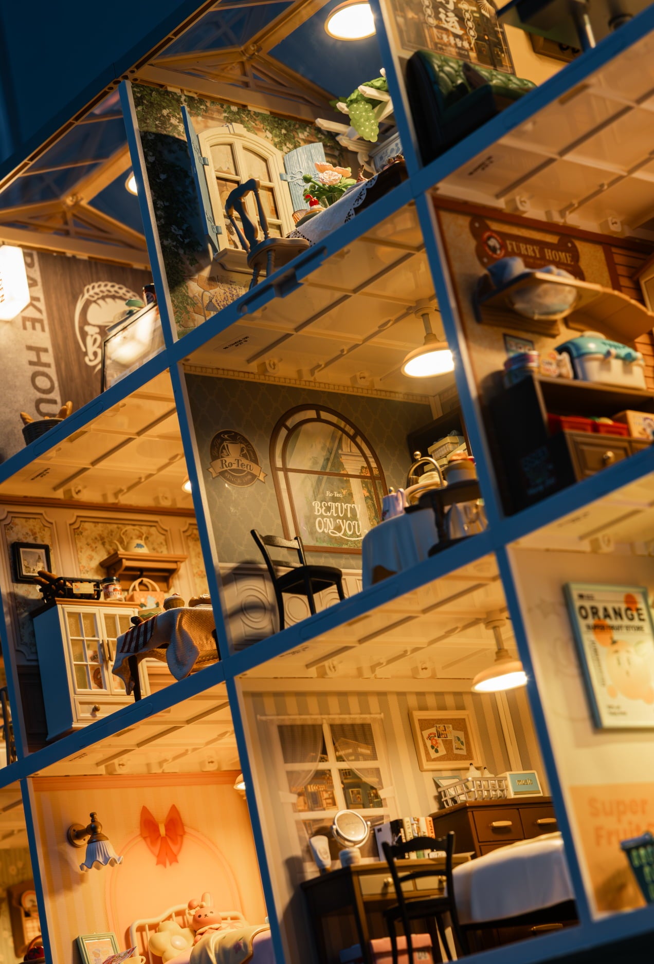 Tall blue dollhouse cutaway revealing several warmly lit rooms and staircases
